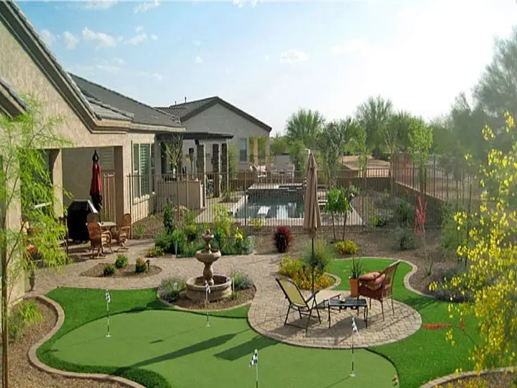 A well-maintained backyard features a putting green, a small fountain, patio furniture, and landscaping that offers a natural look. In the background, there's a swimming pool surrounded by a safety fence next to a residential house. Plants and trees dot the surface of this low-maintenance oasis.